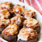 A white serving dish of Italian stuffed mushrooms topped with melted mozzarella cheese on a red and white cloth napkin.