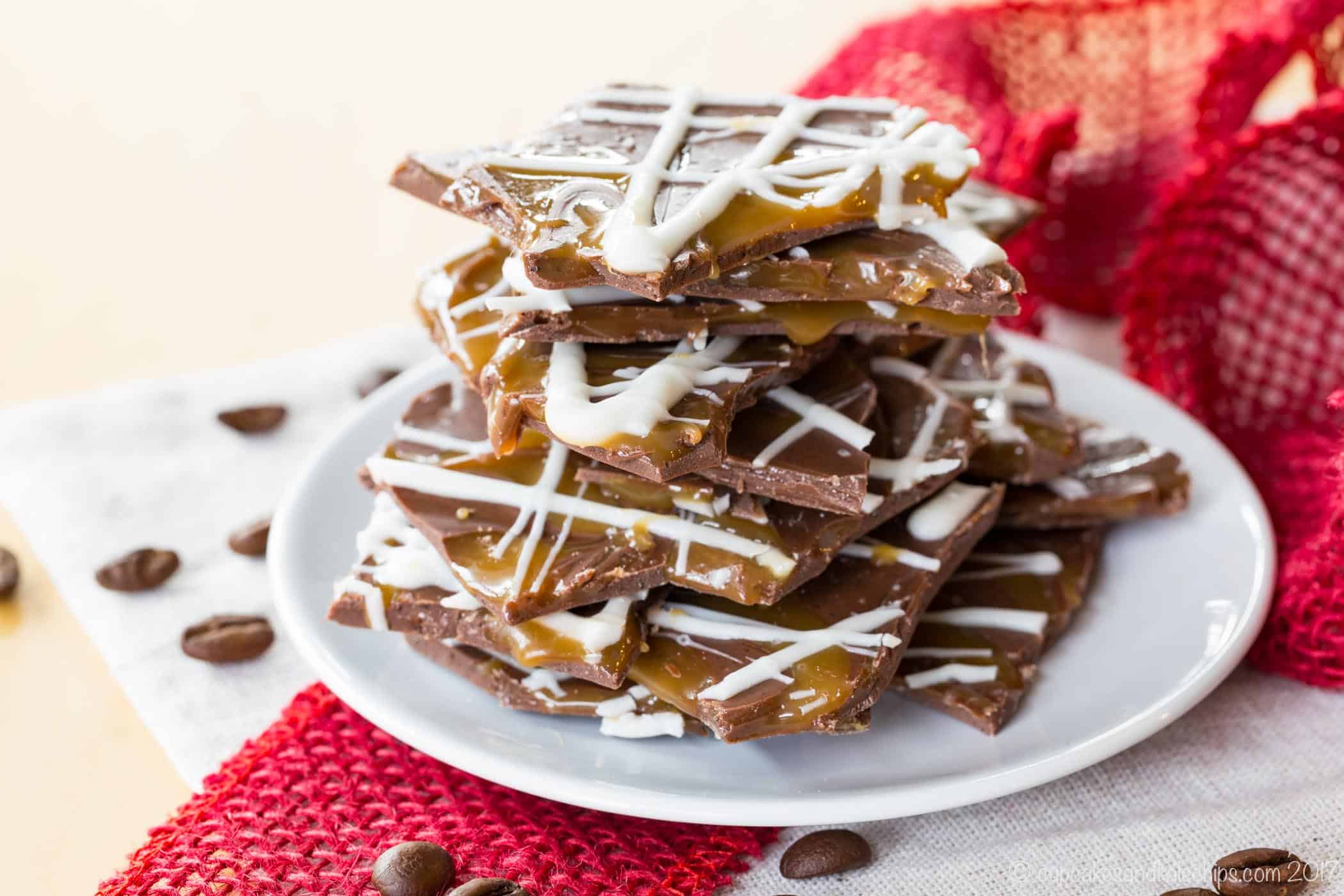 A stack of pieces of Salted Caramel Mocha Chocolate Bark on a white plate surrounded by ribbon and coffee beans.