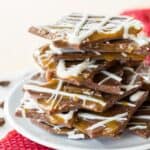 A stack of chocolate bark on a white plate surrounded by ribbon and coffee beans with text overlay that says "Salted Caramel Mocha Chocolate Bark".