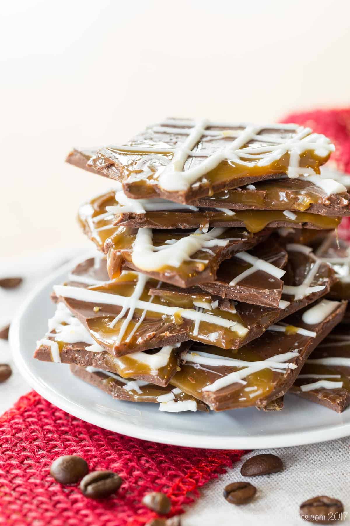 A pile of broken pieces of Salted Caramel Mocha Chocolate Bark on a white plate surrounded by ribbon and coffee beans.