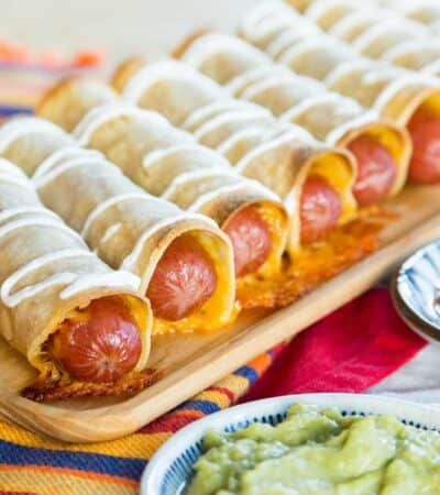 A row of cheesy hot dog taquitos on a wooden platter