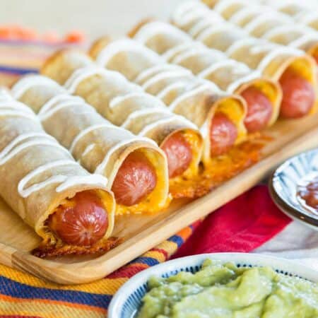 A row of cheesy hot dog taquitos on a wooden platter