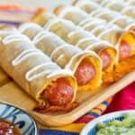 Crispy Hot Dog Taquitos drizzled with sour cream and lined up on a wooden platter.