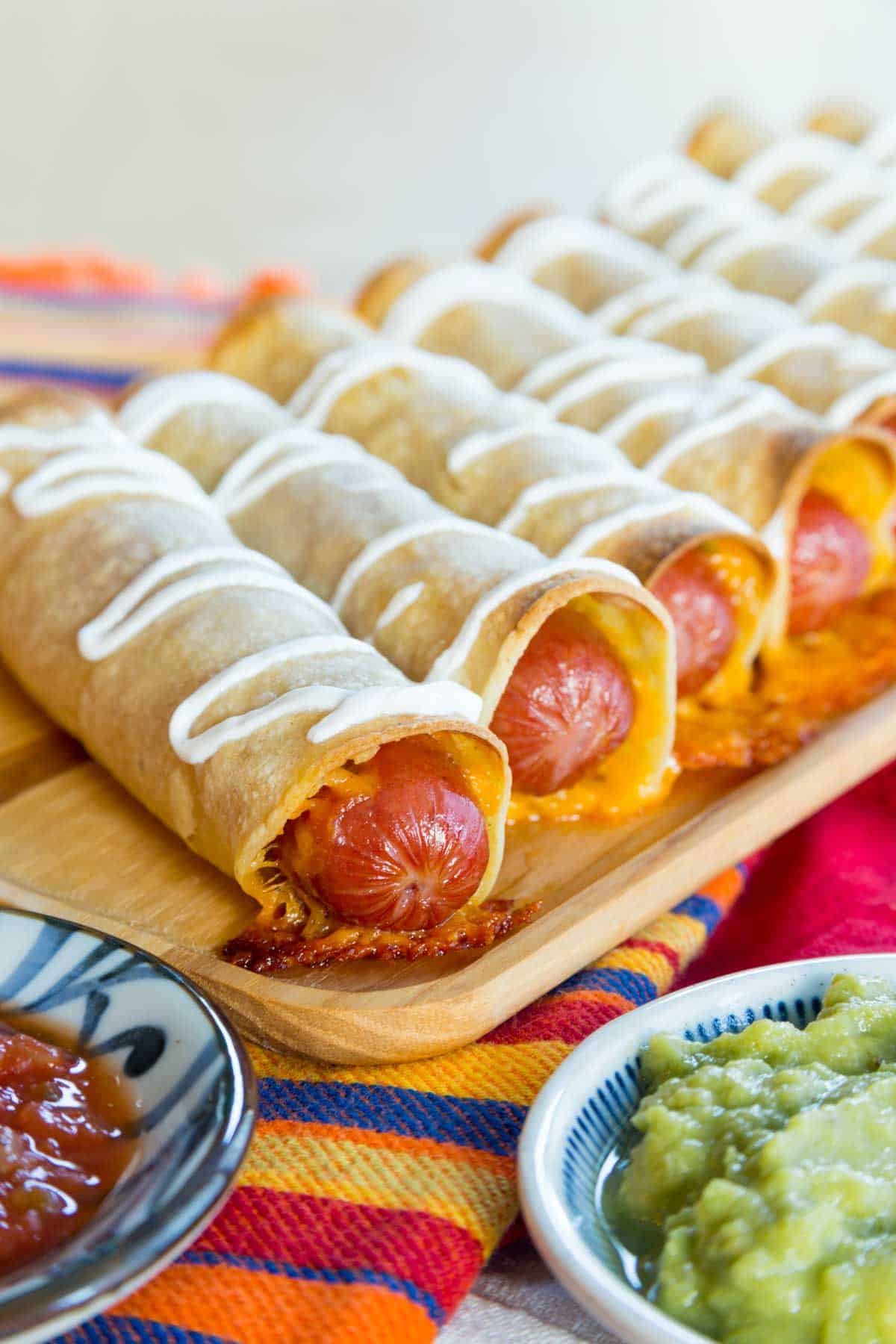 Crispy Hot og Taquitos drizzled with sour cream and lined up on a wooden platter.