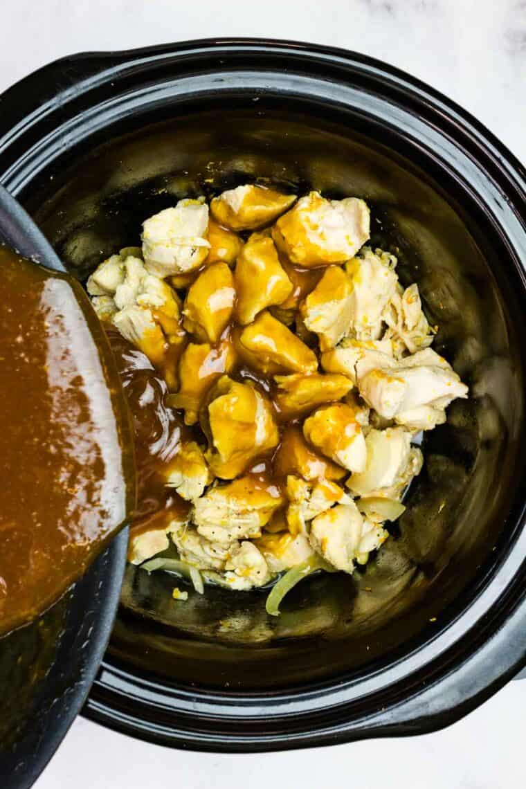Pouring orange sauce over chicken in a slow cooker