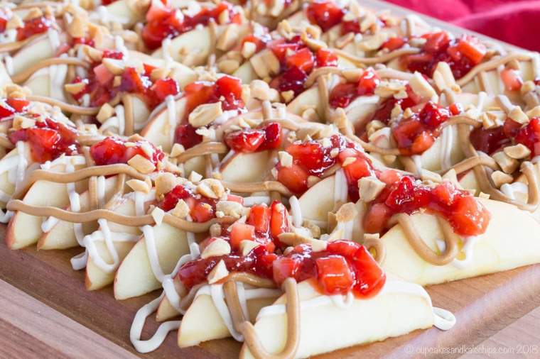 Sliced apples with peanut butter, strawberry salsa, and cheesecake drizzle on a platter