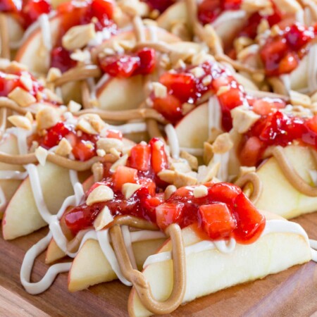 slices of apples topped with peanut butter and strawberry jam on a cutting board