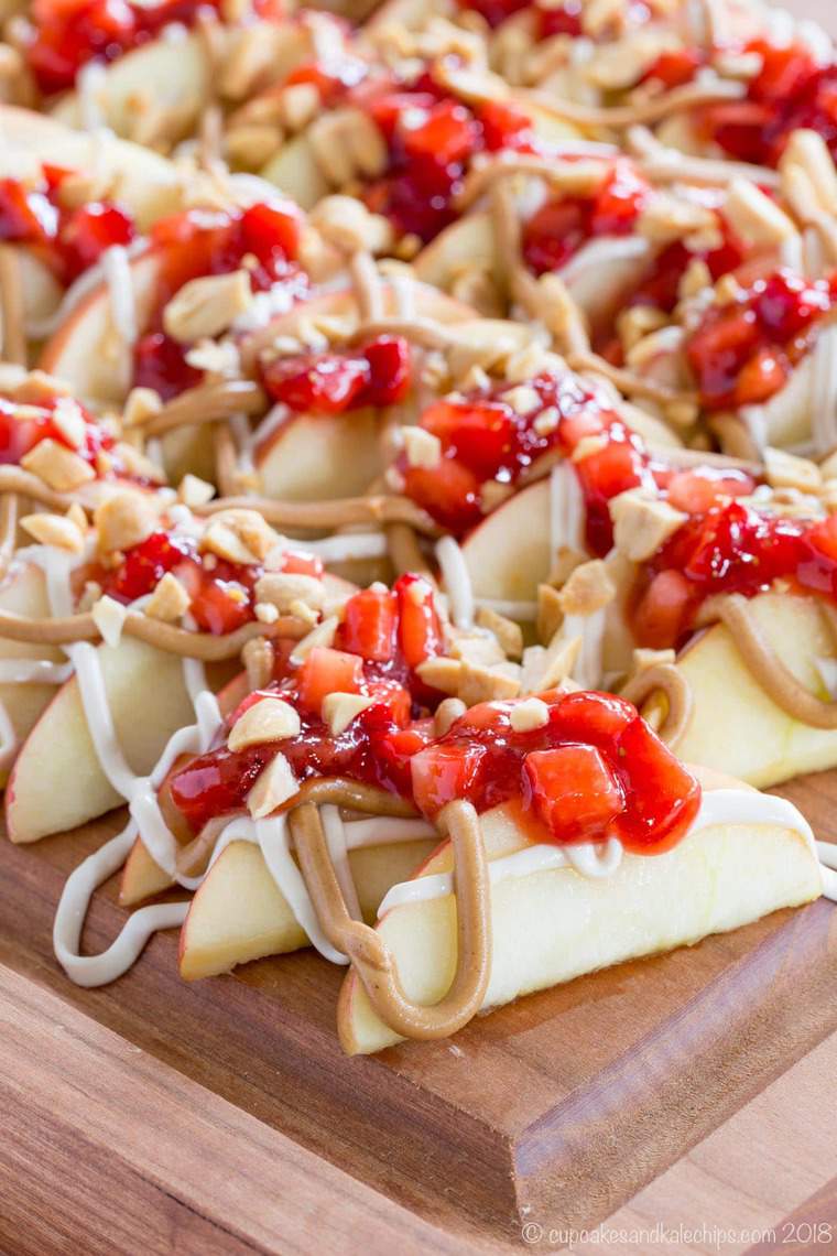 Apple Slices with peanut butter, strawberry salsa, and cream cheese drizzle on a cutting board