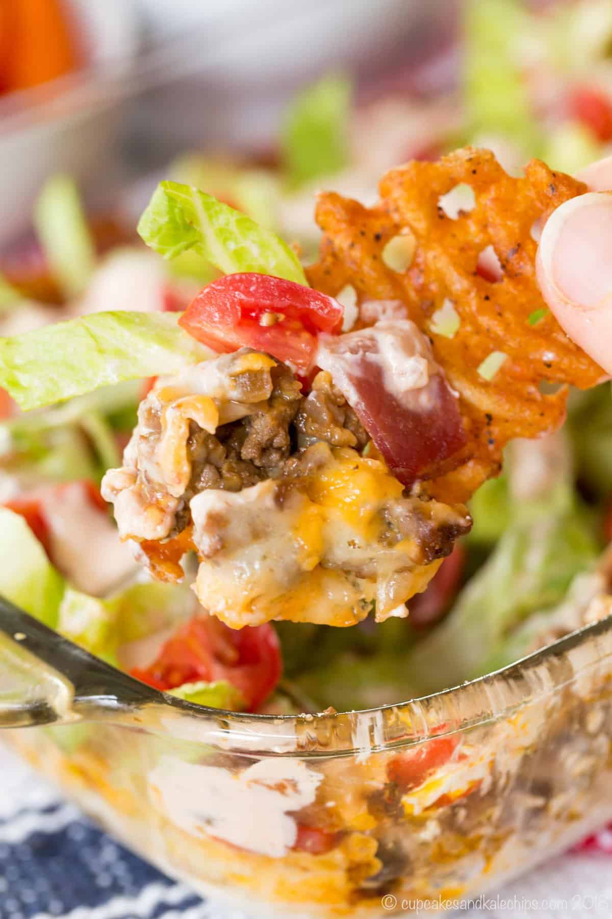 A waffle french fry being held up with melted cheese, cooked beef, bacon, lettuce, and tomato on it.