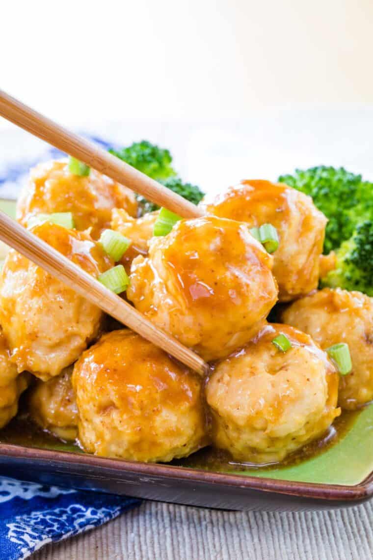 Chopsticks are used to pick up a chicken meatball coated in homemade General Tso's sauce.