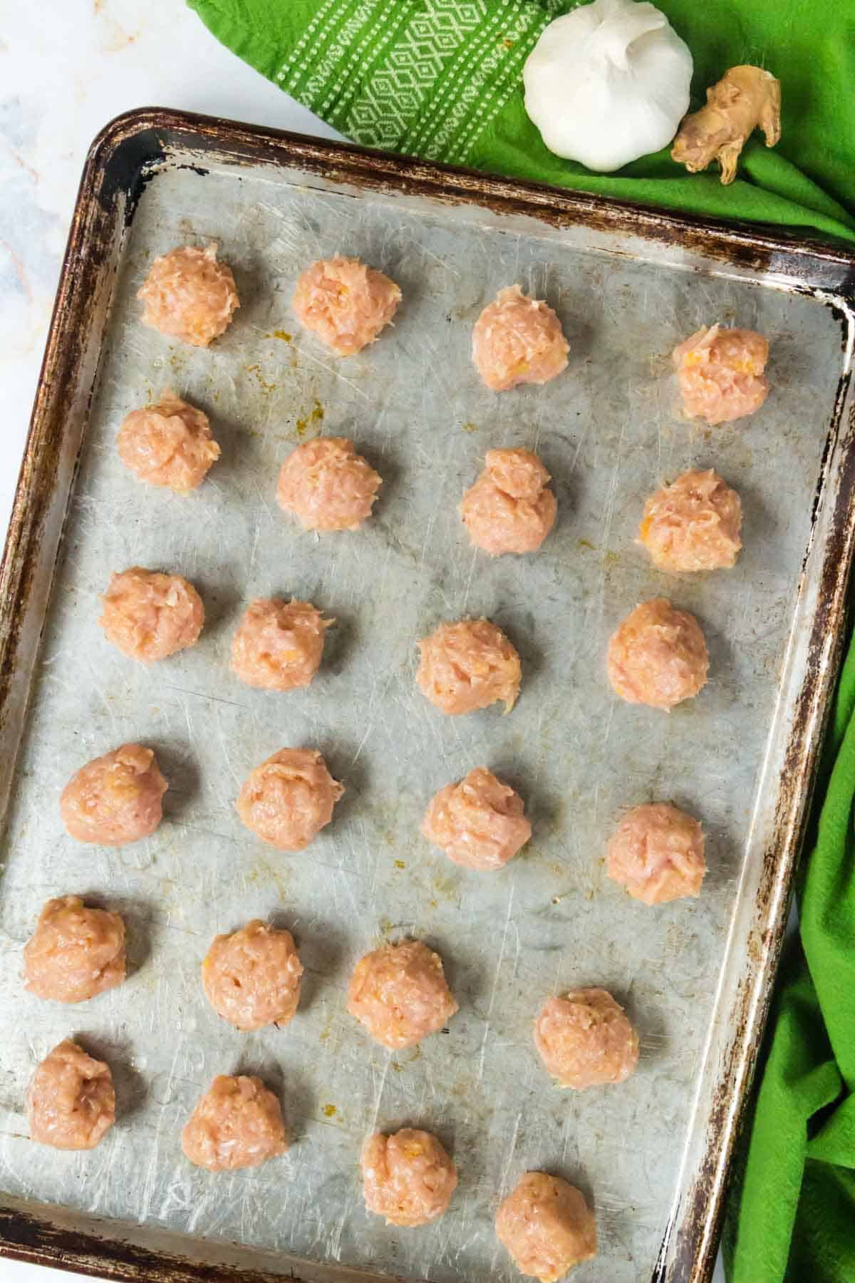 Rolled chicken meatballs laid out on a baking sheet.