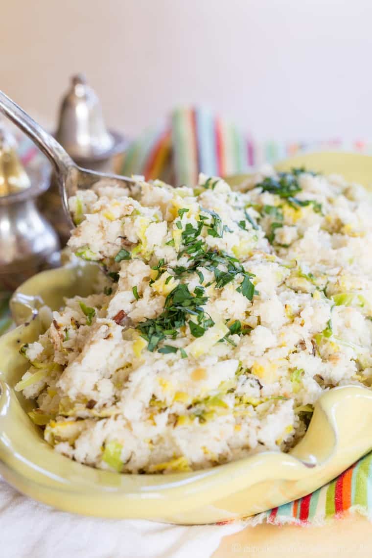 A spoon scoops up cauliflower colcannon from a serving bowl.