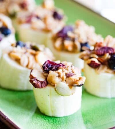 A green plate with banana pieces topped with peanut butter and granola.