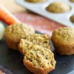 Three mini muffins on a slate platter with one split in half with text overlay that says "Gluten Free Carrot Zucchini Muffins".