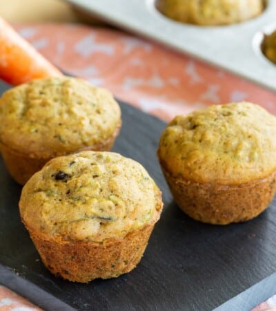 three gluten free mini vegetable muffins on a tray with a carrot and zucchini nearby