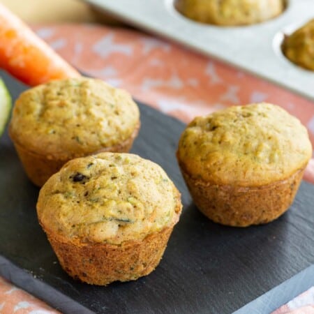 three gluten free mini vegetable muffins on a tray with a carrot and zucchini nearby