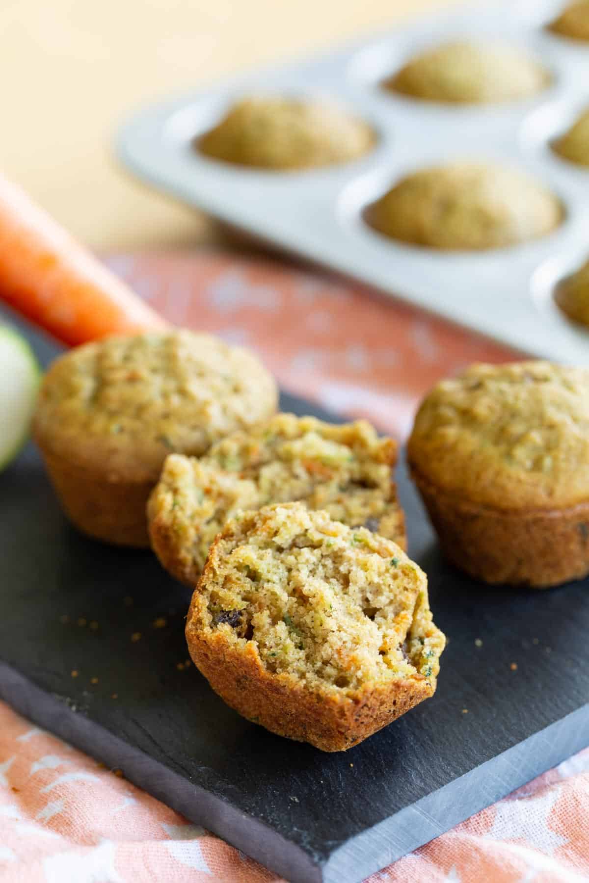 three gluten free carrot zucchini muffins on a slate platter with one split in half