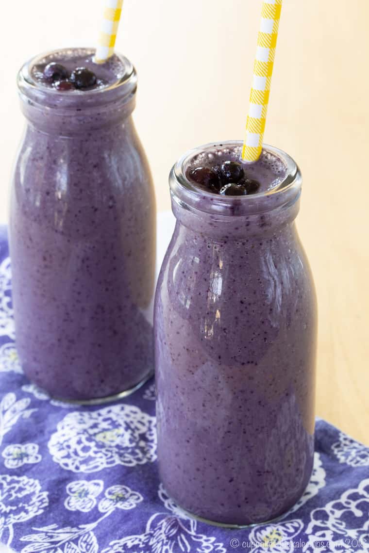 Two Blueberry Almond Butter Smoothies in clear glass milk bottles with yellow and white paper straws