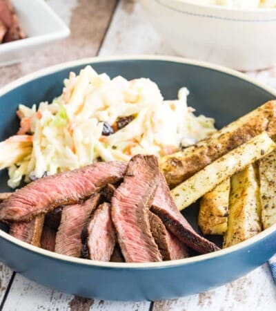 sliced flat iron steak, potatoes, and coleslae on a blue plate with cloth napkins and blue plastic utensils