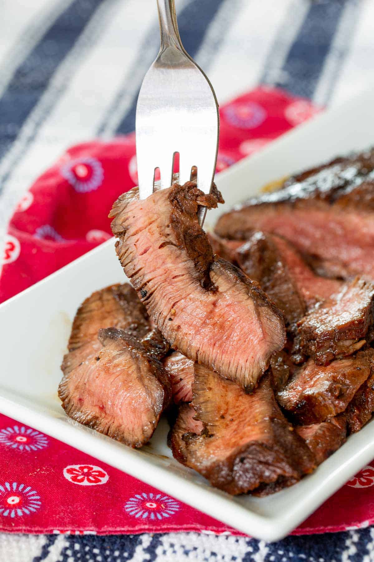 fork picking up a slide of grilled flat iron steak from the rest of the steak on a white plate