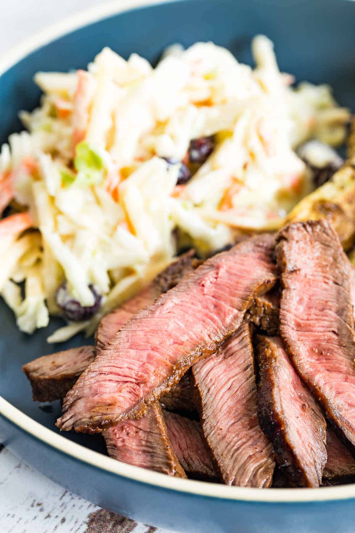 slices of steak on a blue plate with coleslaw