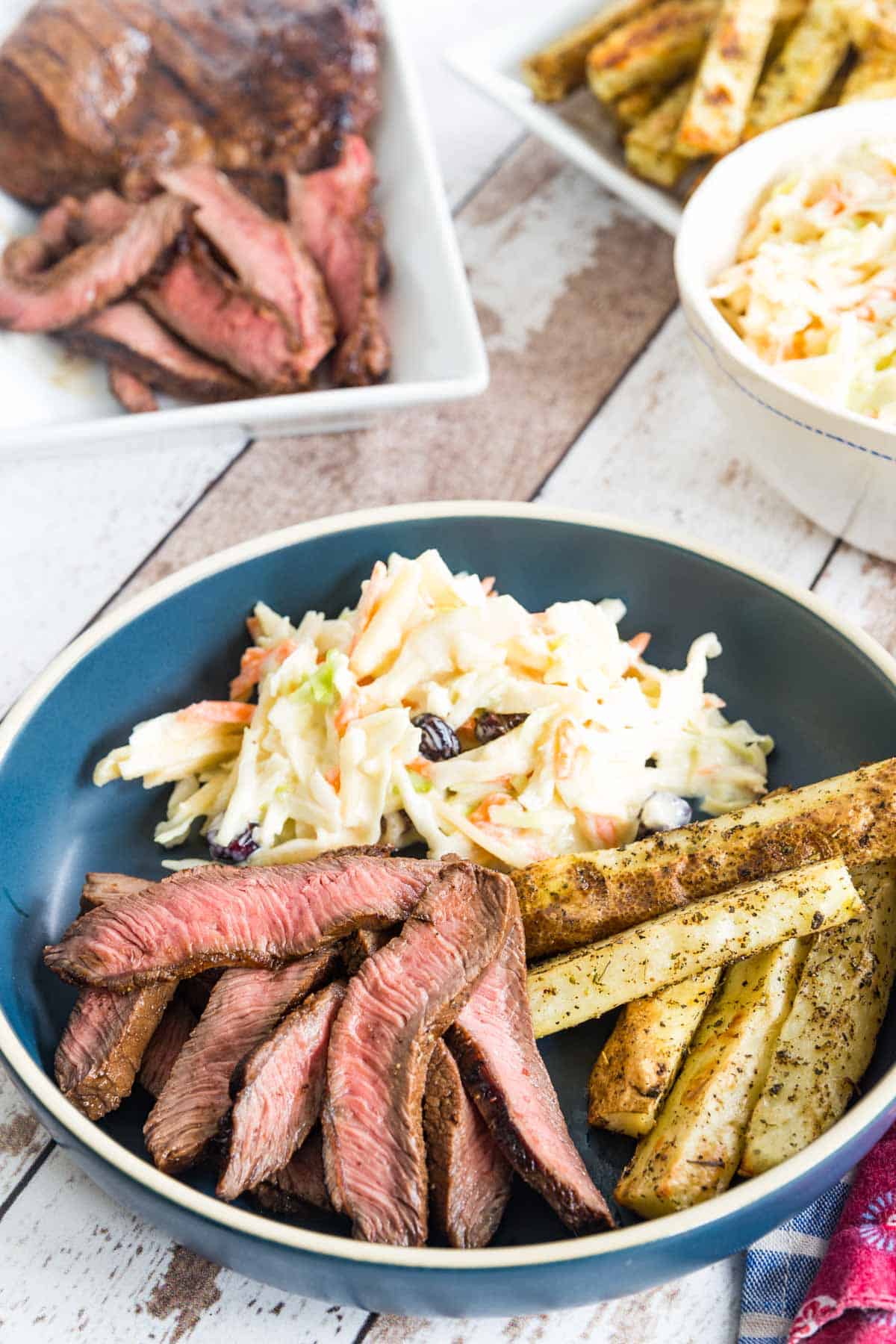 blue plate with sliced steak, baked french fries, and coleslaw