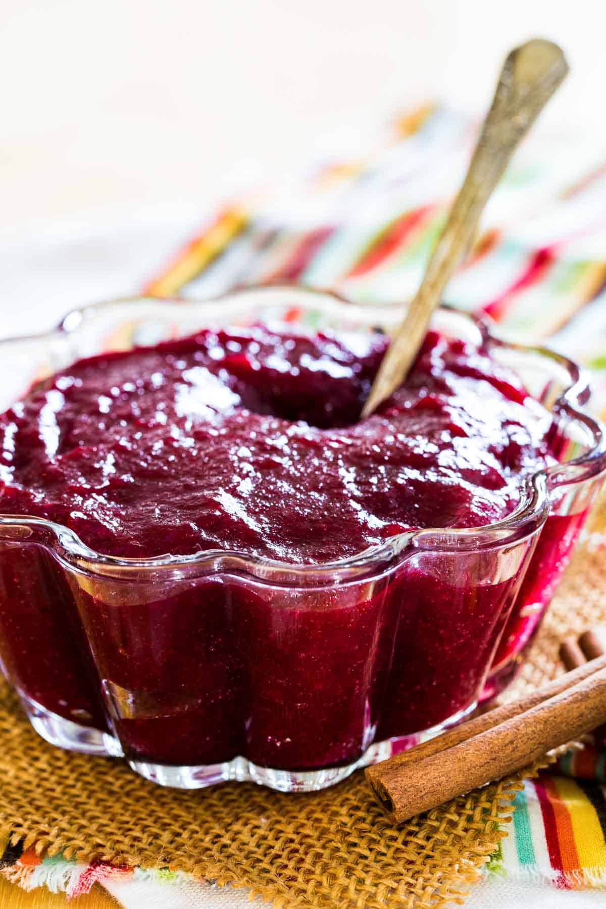 Cinnamon orange cranberry sauce in a scalloped glass bowl with a spoon.