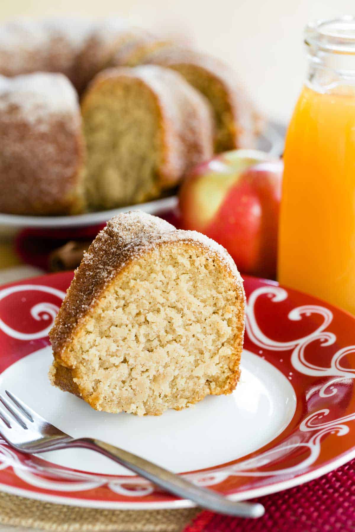 a slice of gluten free apple cider doughnut cake on a white plate with a red scroll design