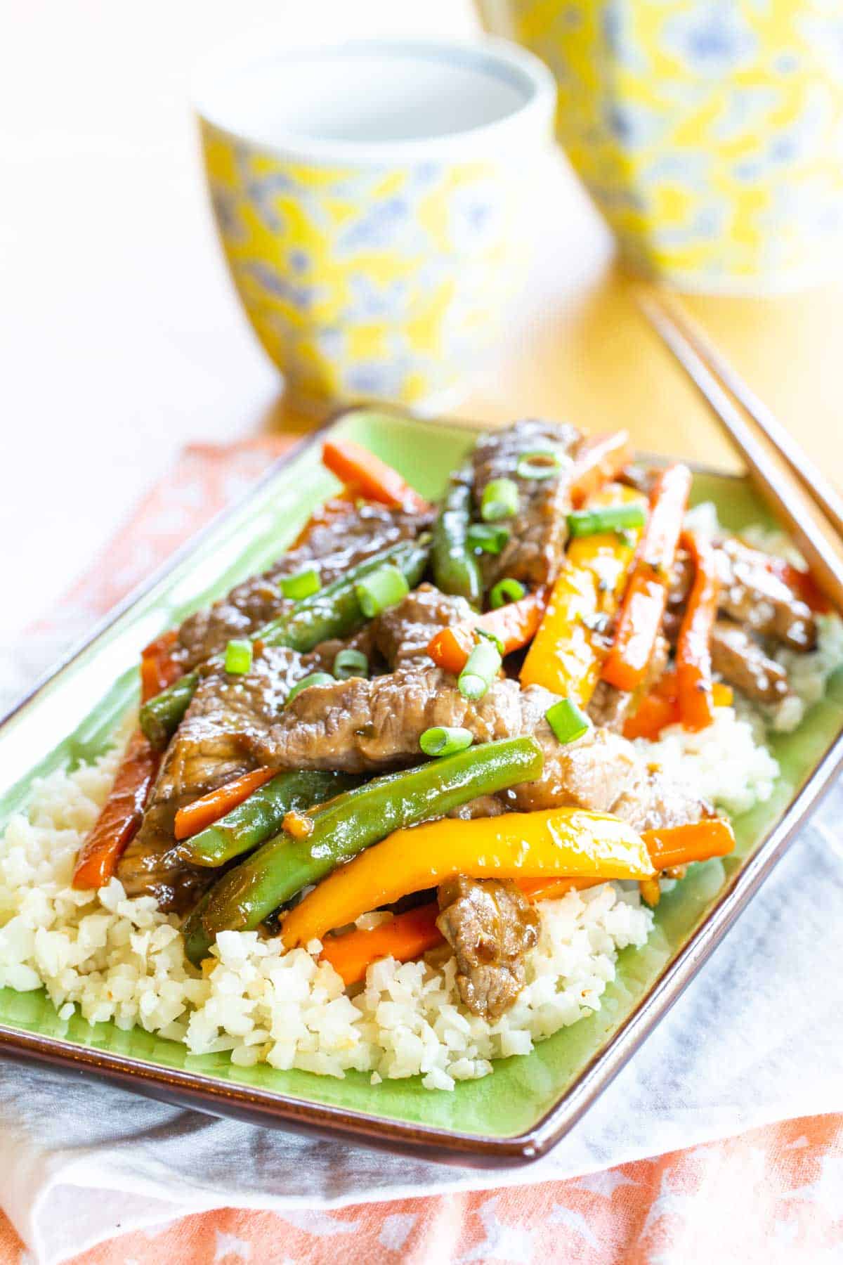 Vegetable Beef Stir fry served over rice on a rectangular green plate.