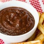 A white bowl of balsamic ketchup surrounded by french fries.