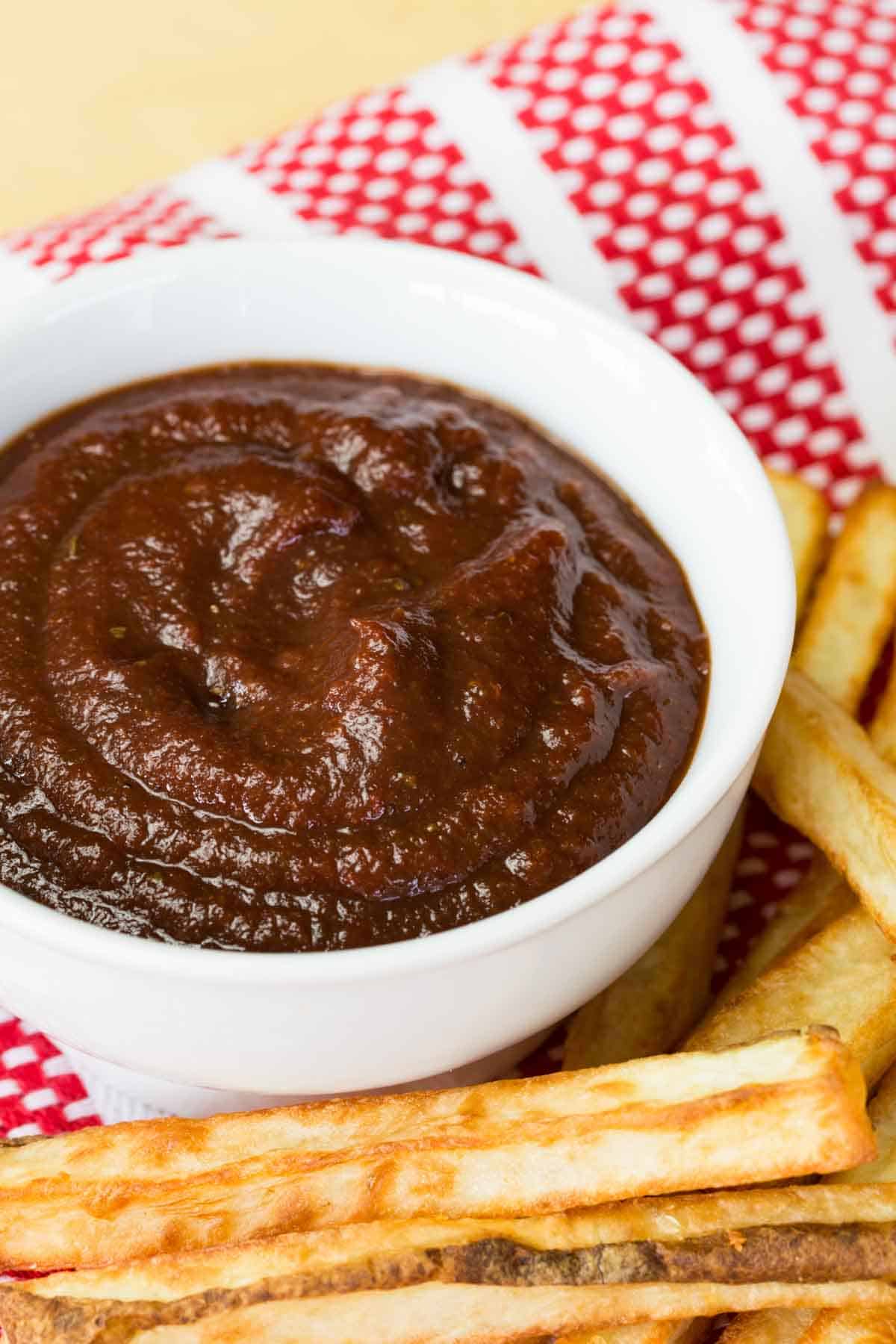 A white bowl of balsamic ketchup surrounded by french fries.