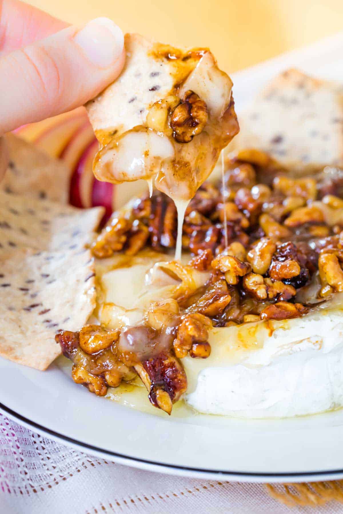 Melty baked brie and nuts dripping off of a cracker over the entire wheel served on a plate.
