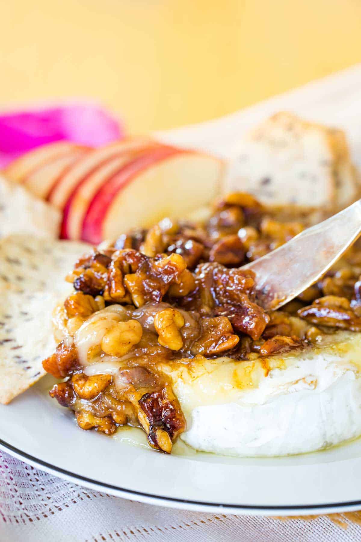 A small spreader starting to scoop up some melty baked brie topped with honey-glazed walnuts and pecans.