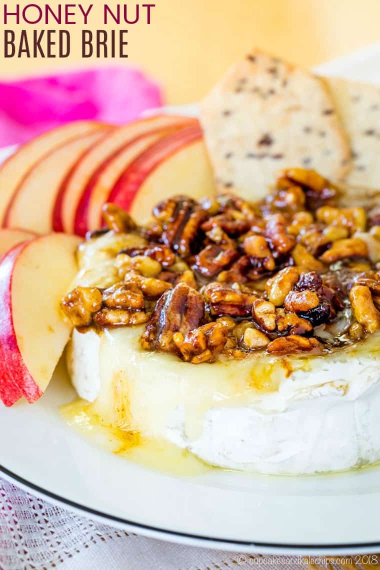 Baked brie covered with honey glazed nuts and next to apple slices and crackers.