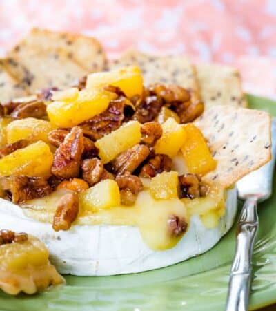 Pineapple and pecan-topped baked brie on a green plate with a small spreader knife.