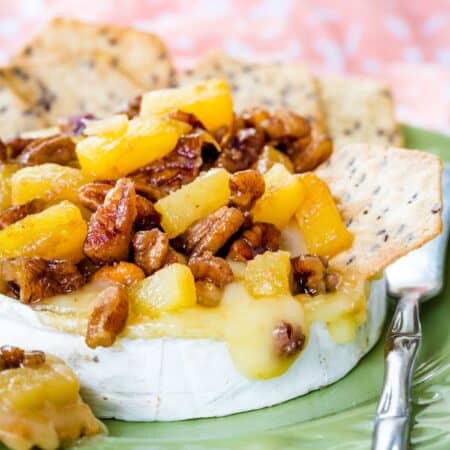 Pineapple and pecan-topped baked brie on a green plate with a small spreader knife.