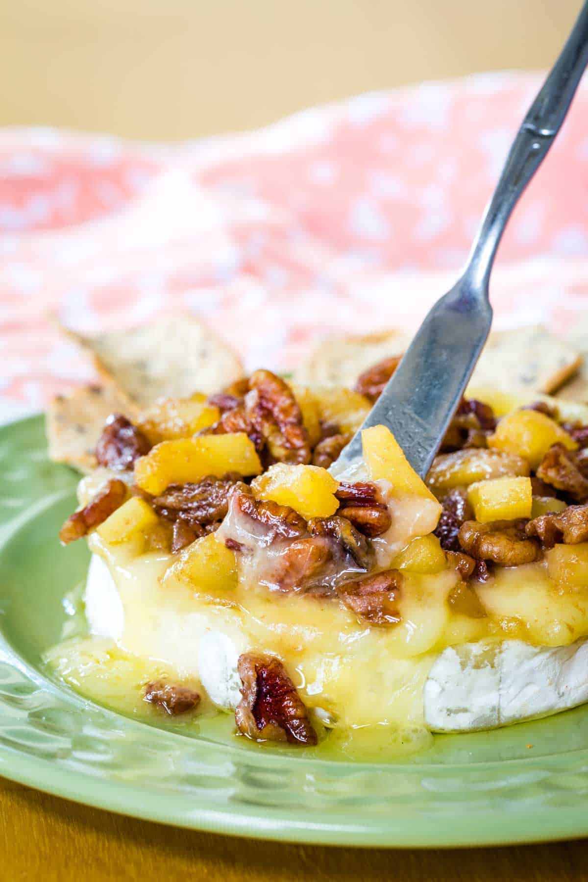 A small spreader knife in a melty wheel of Brie topped with pineapples and pecans.