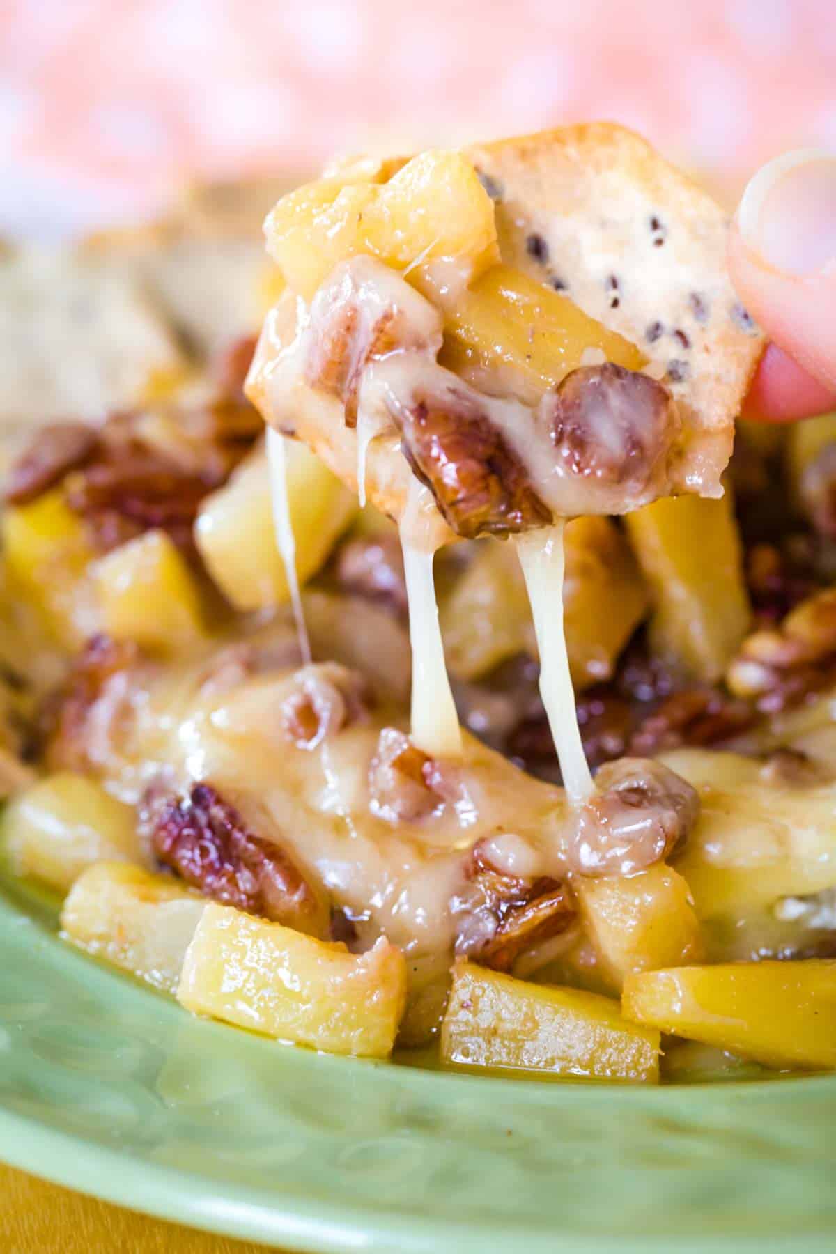 A cracker with some pineapple tidbits and chopped pecans on it with melty Brie cheese dripping off.