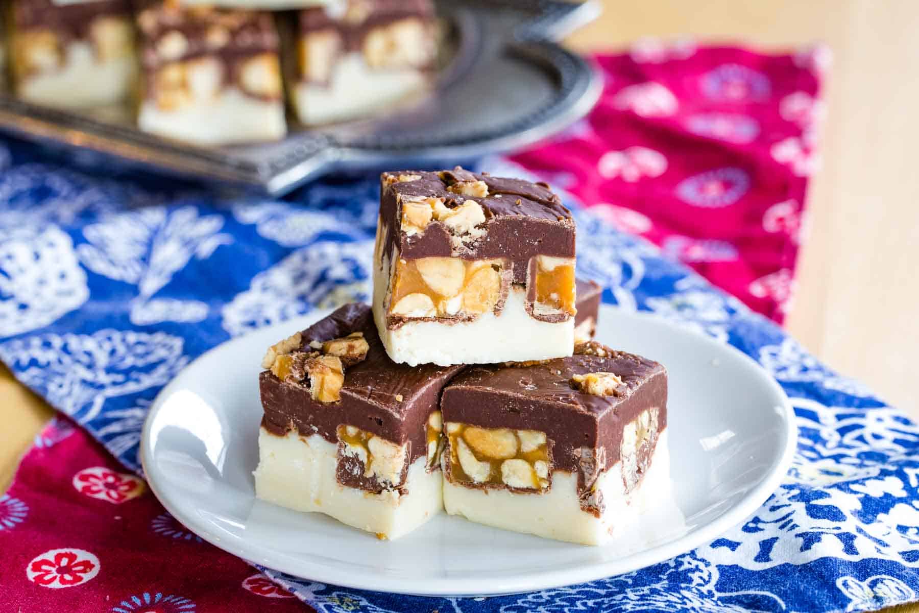 Pieces of Snickers Fudge on a plate on top of two criss-crossed cloth napkins.