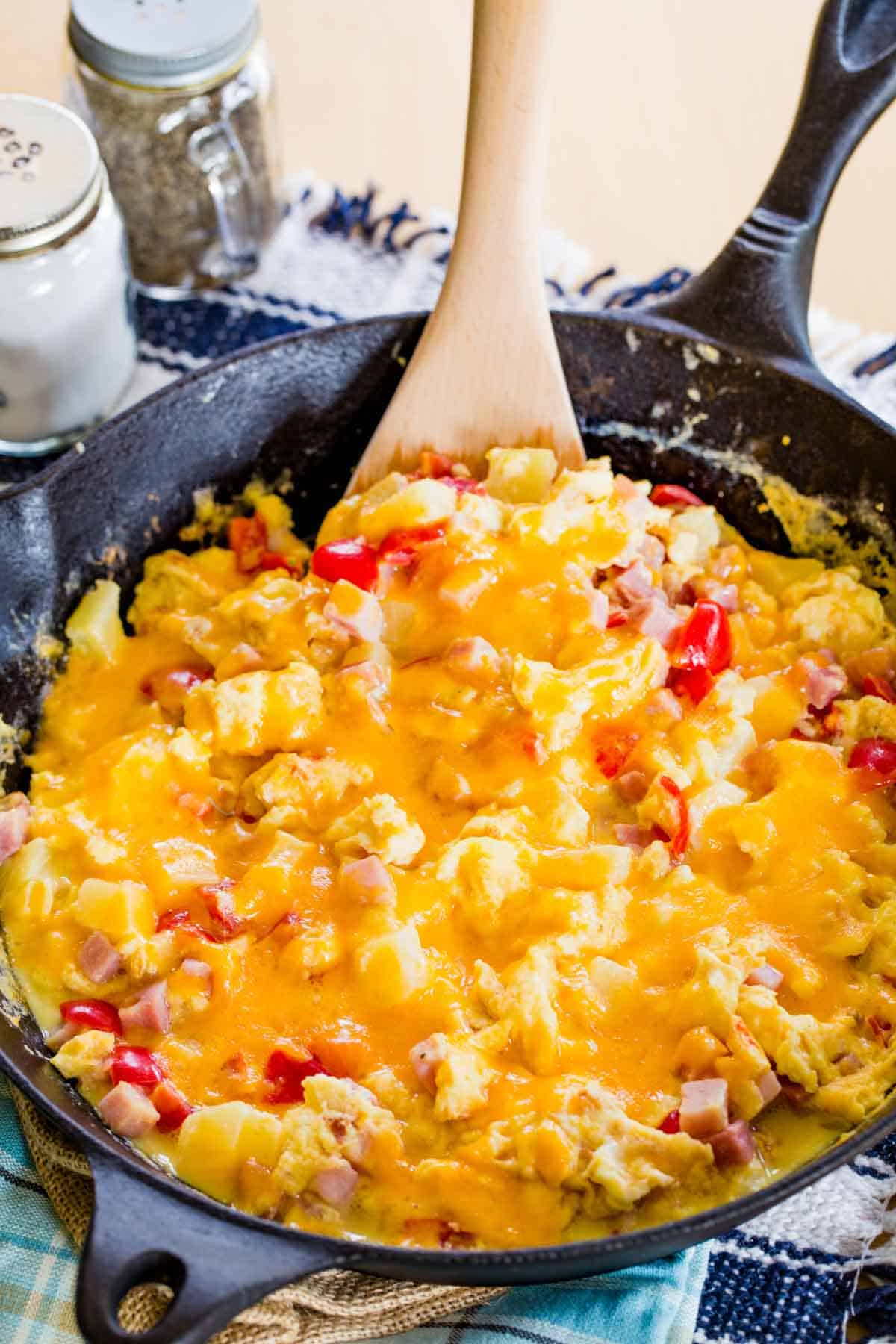 An egg scrambled with cheese, ham, tomato, and pineapple in a cast iron skillet.