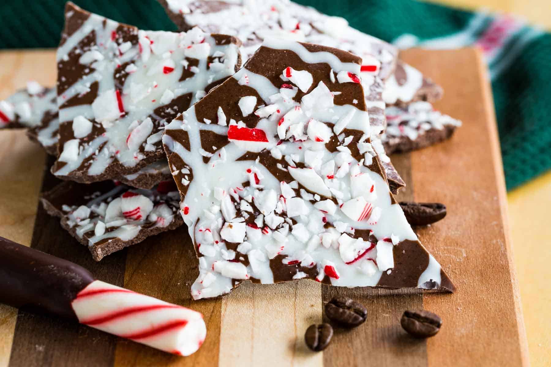 Pieces of Peppermint Mocha Chocolate Bark on a cutting board with a candy cane and coffee beans.