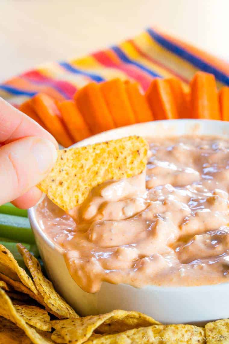 A tortilla chip being dipped into buffalo dip.