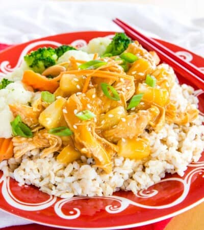 Pineapple Teriyaki Chicken Over rice on a red and white plate with red chopsticks