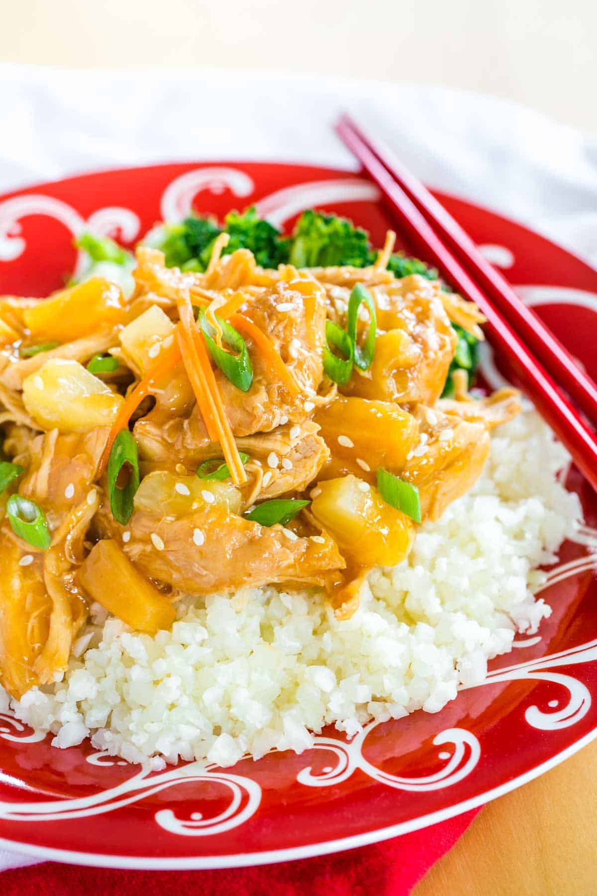 teriyaki chicken over cauliflower rice on a red plate with white decorative swirls