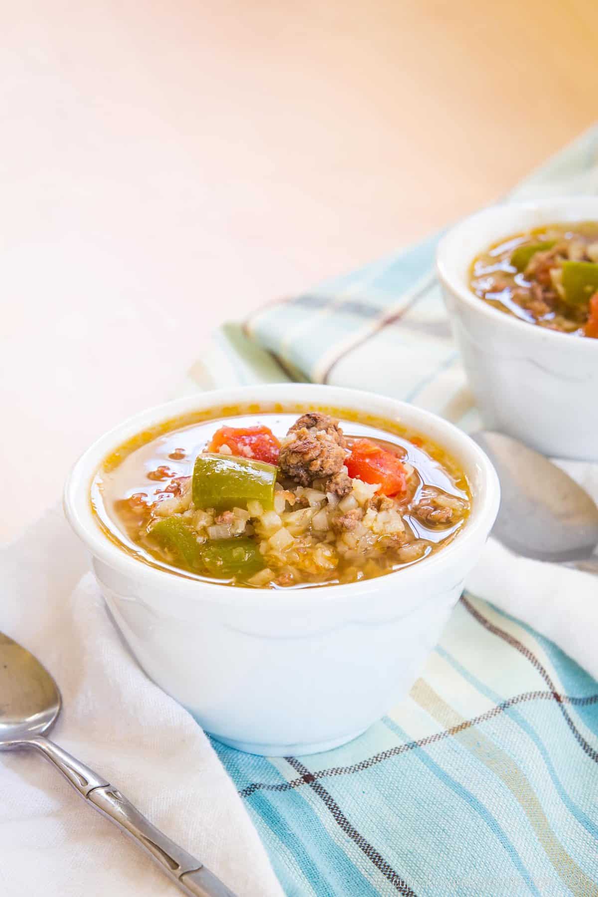 A bowl of stuffed pepper soup with a spoon on a cloth napkin and another one off to the side in the background.