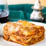 A slice of lasagna and a fork on a plate with a textured edge with text overlay that says "World's Best Gluten Free Lasagna".