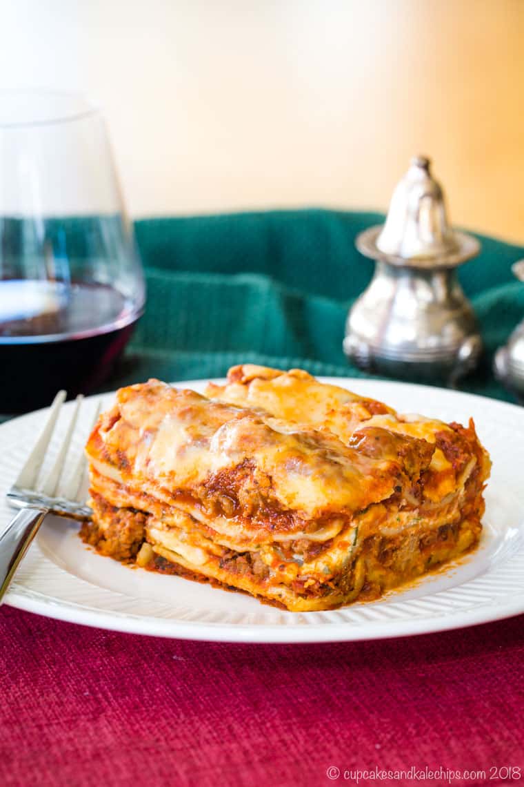 A piece of lasagna on a plate with a fork resting next to it.