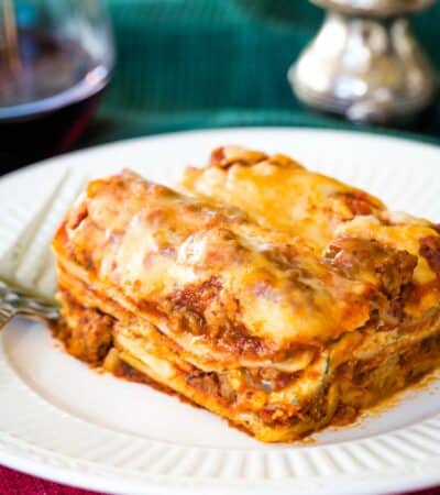 Homemade Gluten Free Lasagna on a plate on a red placemat with a glass of red wine and silver salt and pepper shakers.