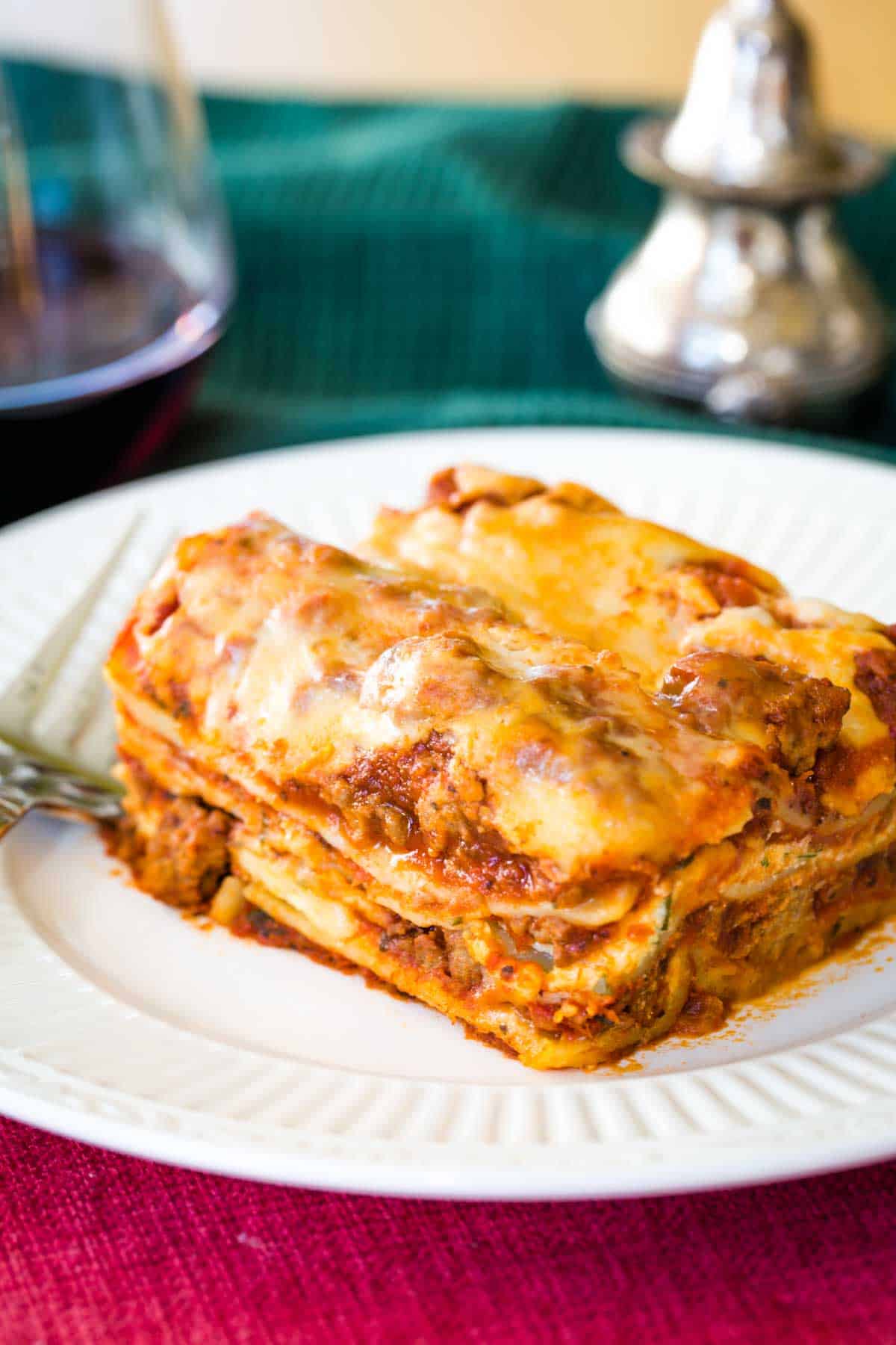 Homemade Gluten Free Lasagna on a plate on a red placemat with a glass of red wine and silver salt and pepper shakers.