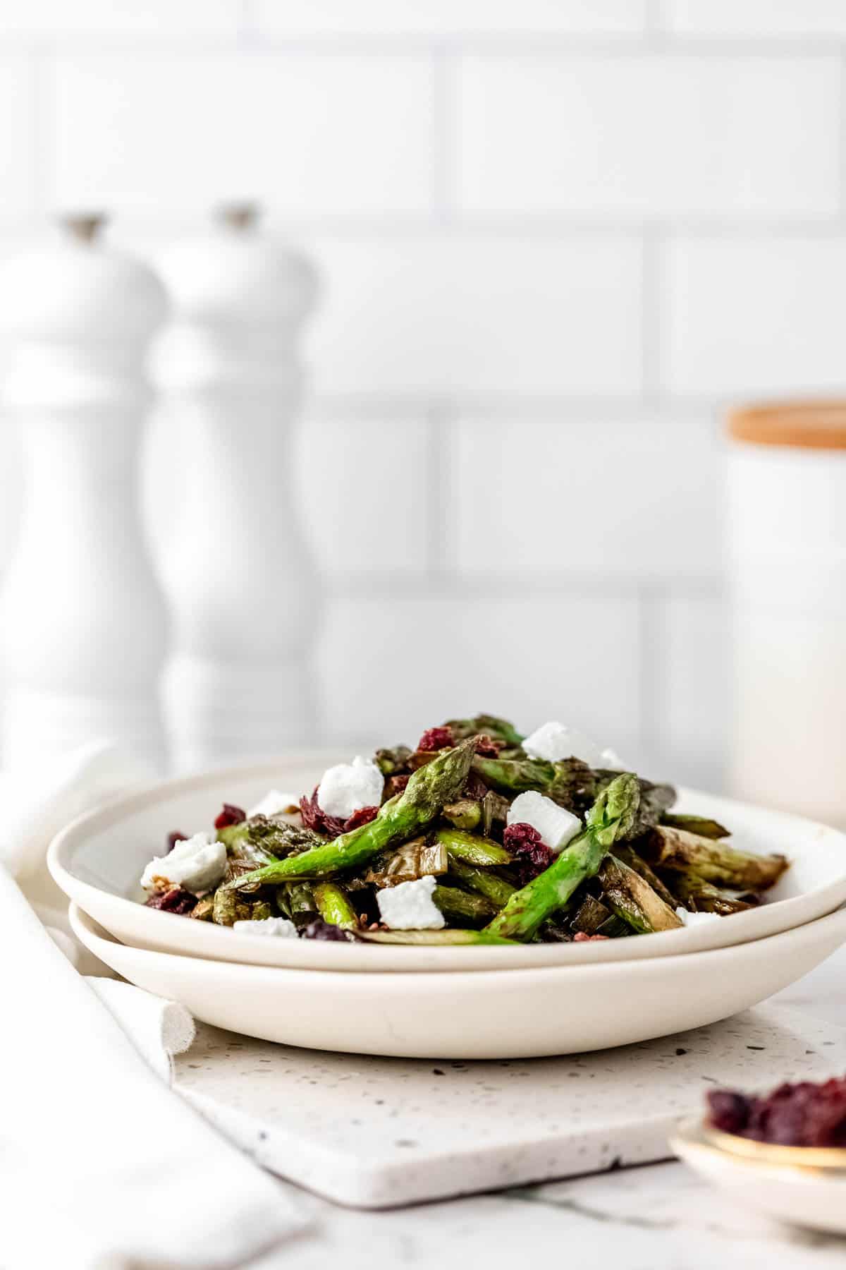 Roasted asparagus salad in a white bowl topped with chunks of goat cheese and dried cherries.